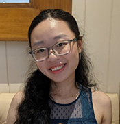 A smiling young woman in glasses sits on a couch