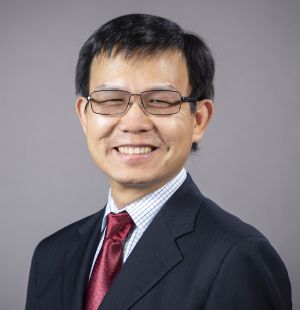 Kai Zhang, smiling and wearing glasses and a suit.