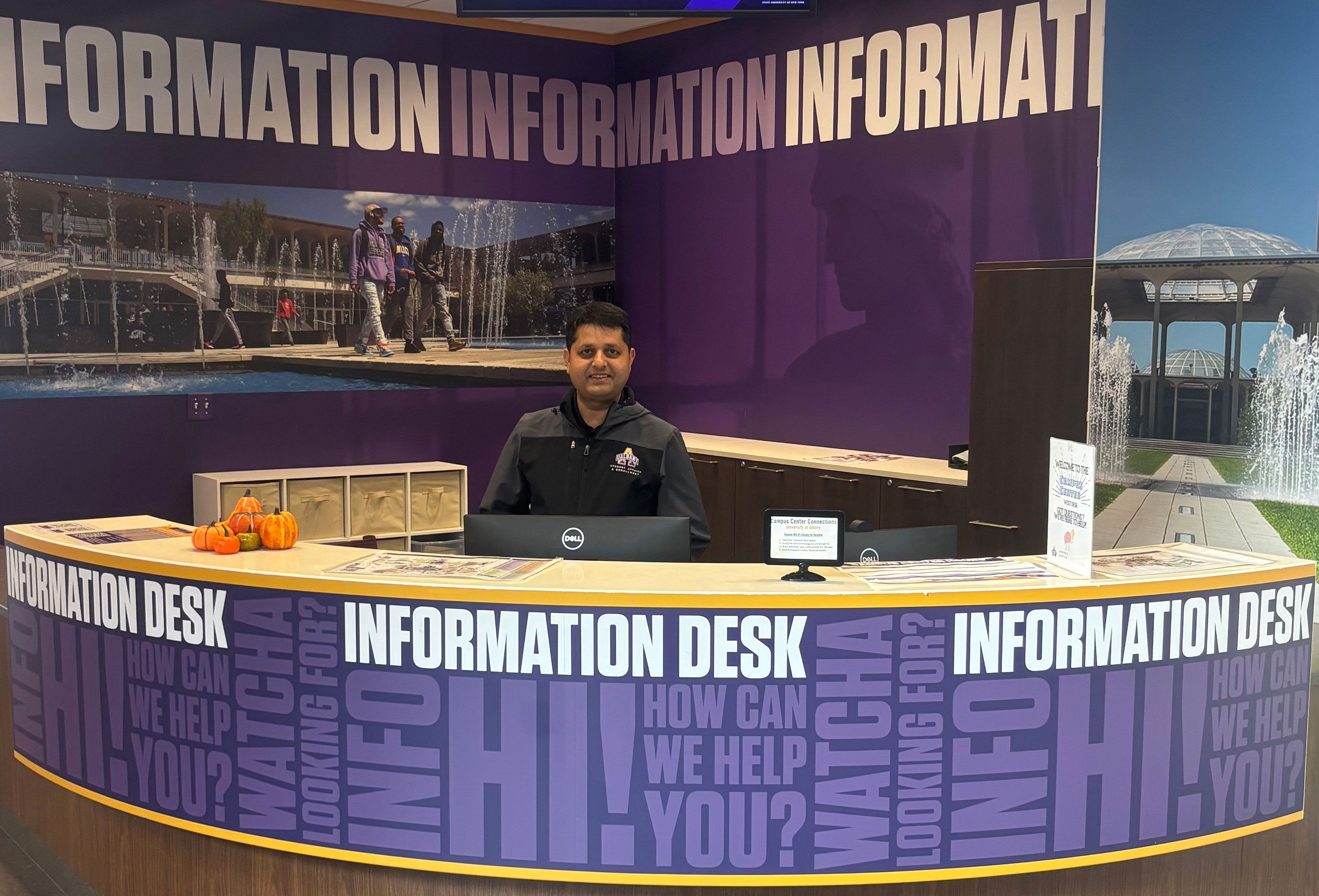 Khem Sedhai smiles as he sits behind a UAlbany information desk on campus.