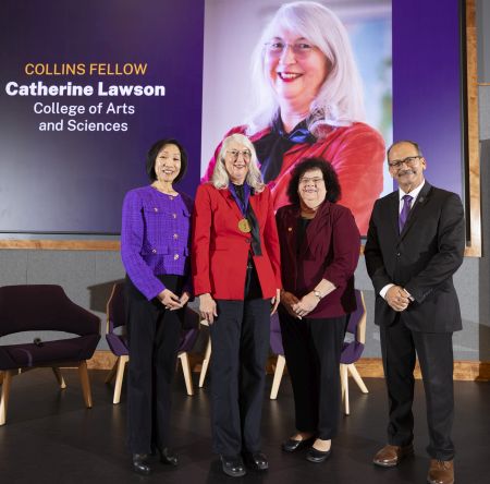 four people stand in front of an image of one of them -- a white-haired soman in a red jacket next to the words "Collins Fellow Catherin Lawson College of Arts and Sciences"