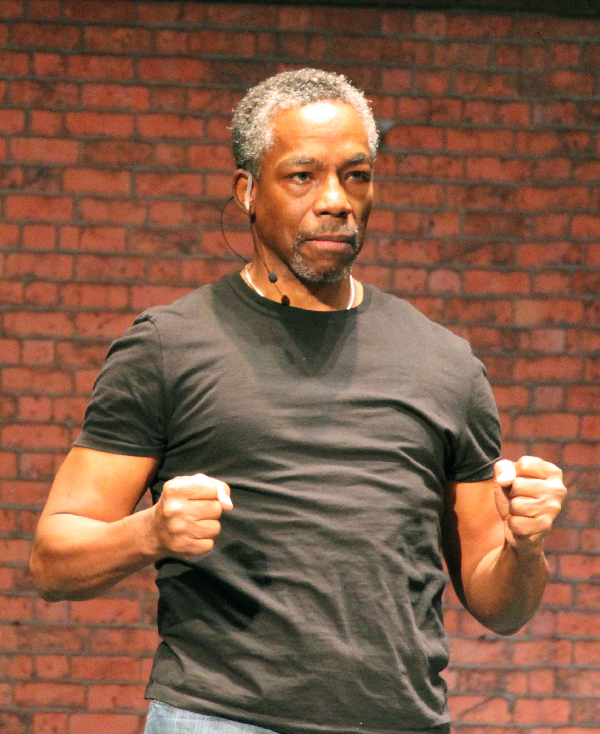 black actor in a dark t-shirt stands with fists clenched by his side
