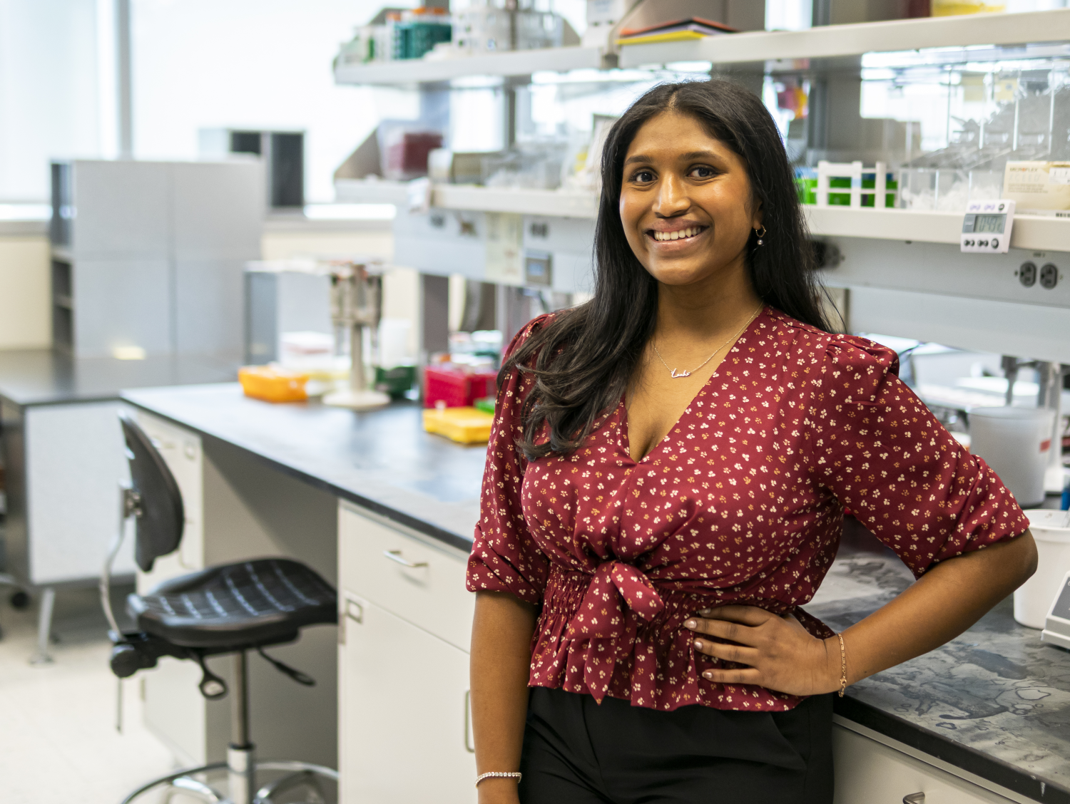 A smiling woman in a brown shirt with dots poses in a lab,