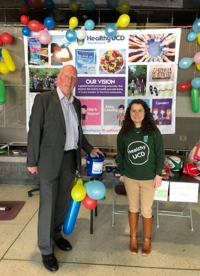 Maeve stands in front of a poster of her project, wearing a University College Dublin green sweatshirt.