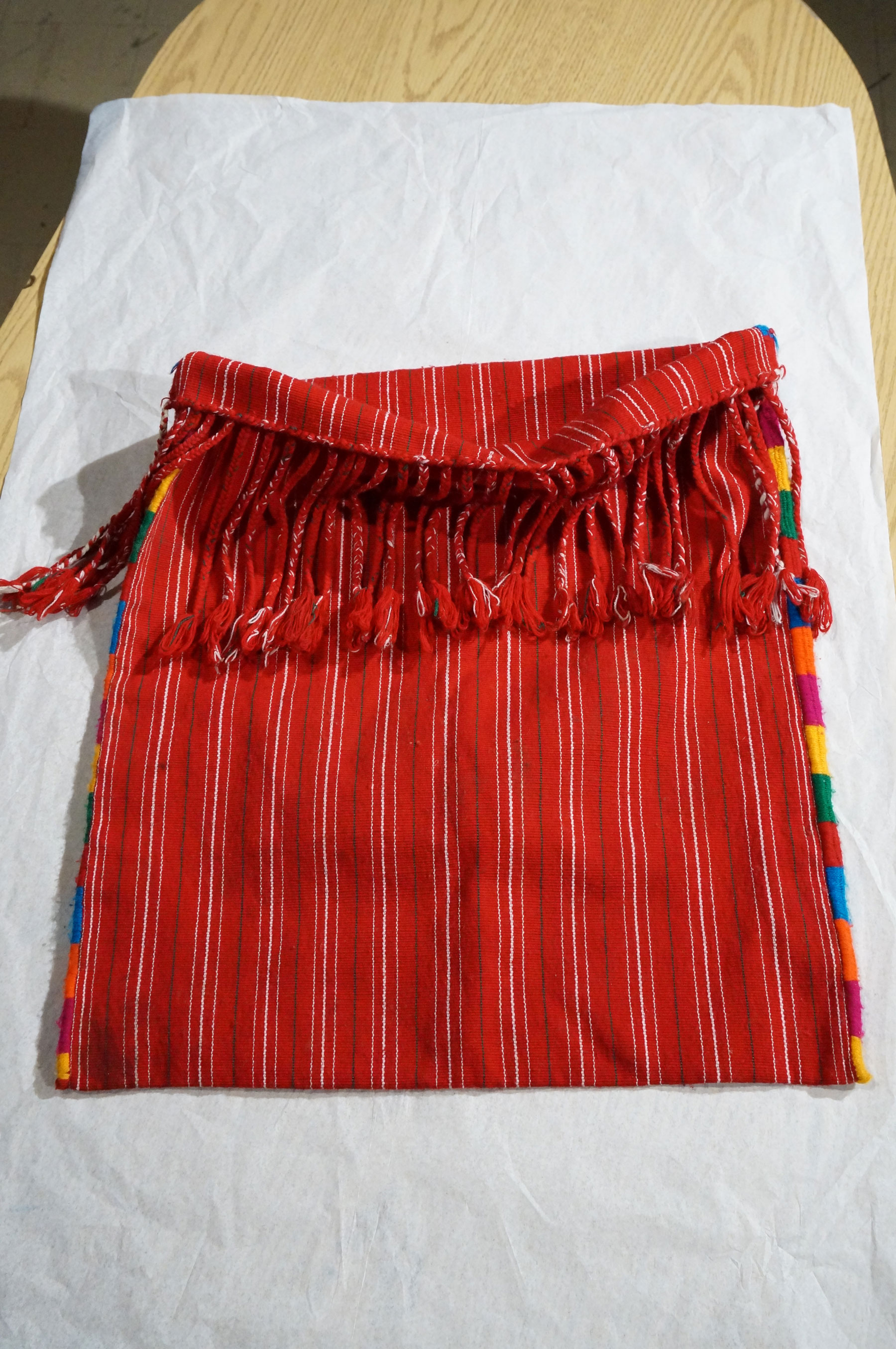 A man's red bag with white stripes, red rope fringe and colorful stitching.
