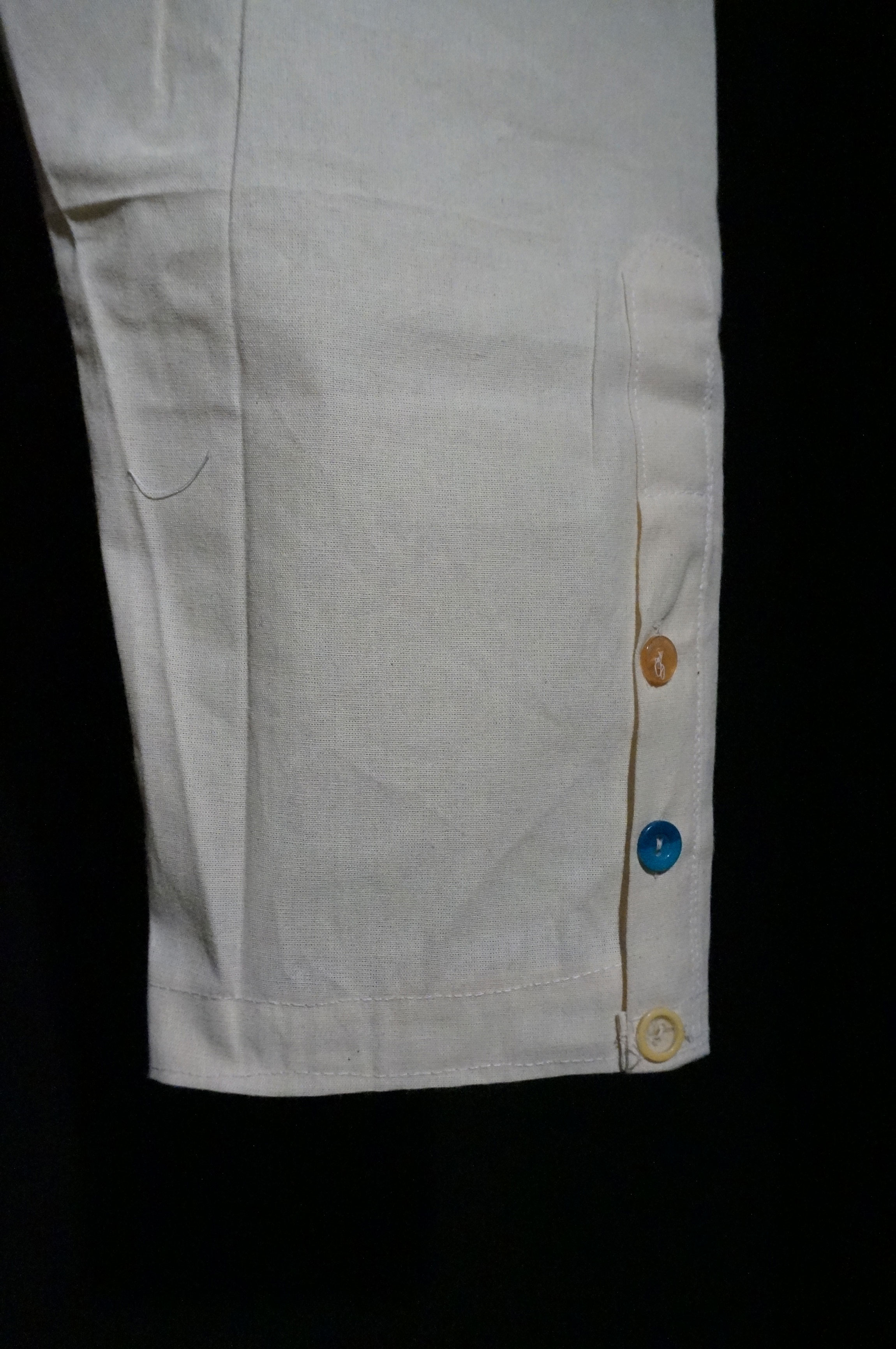 Close up of a man's white linen pants, with multicolored buttons along the ankle.