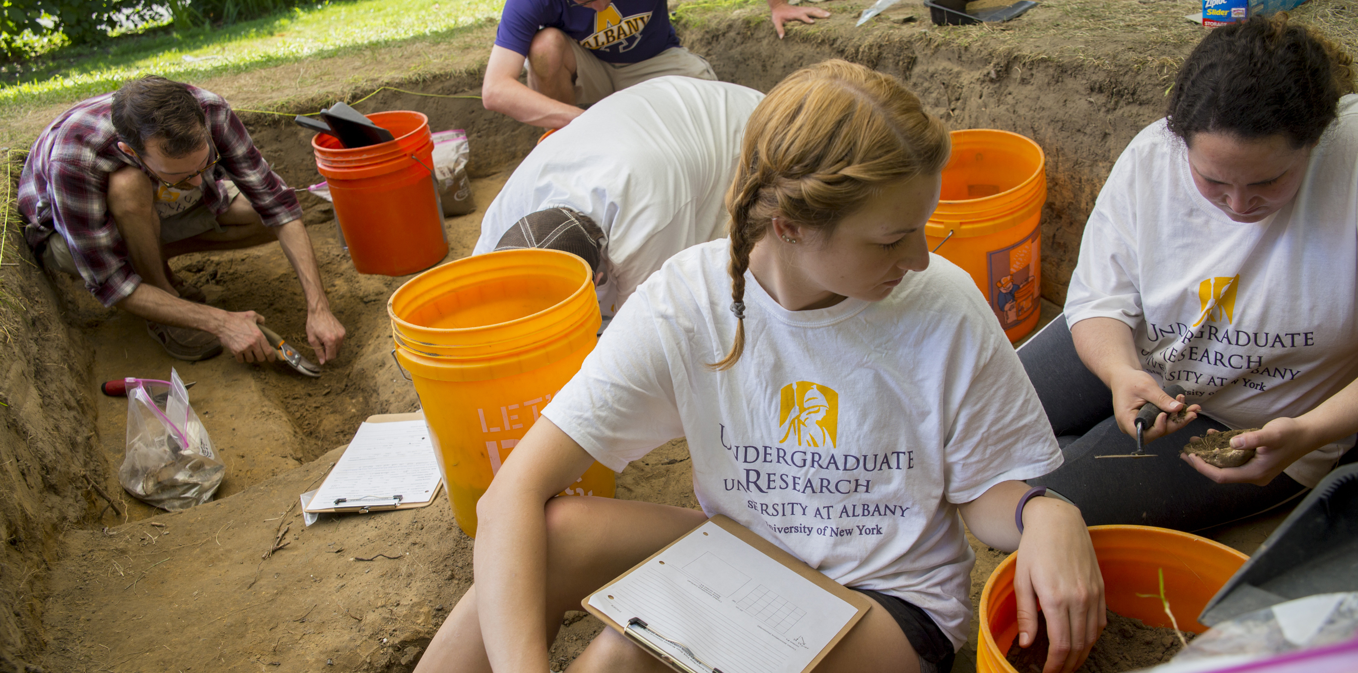Five students wearing Undergraduate Research t-shirts excavate artifacts at the archaeology dig