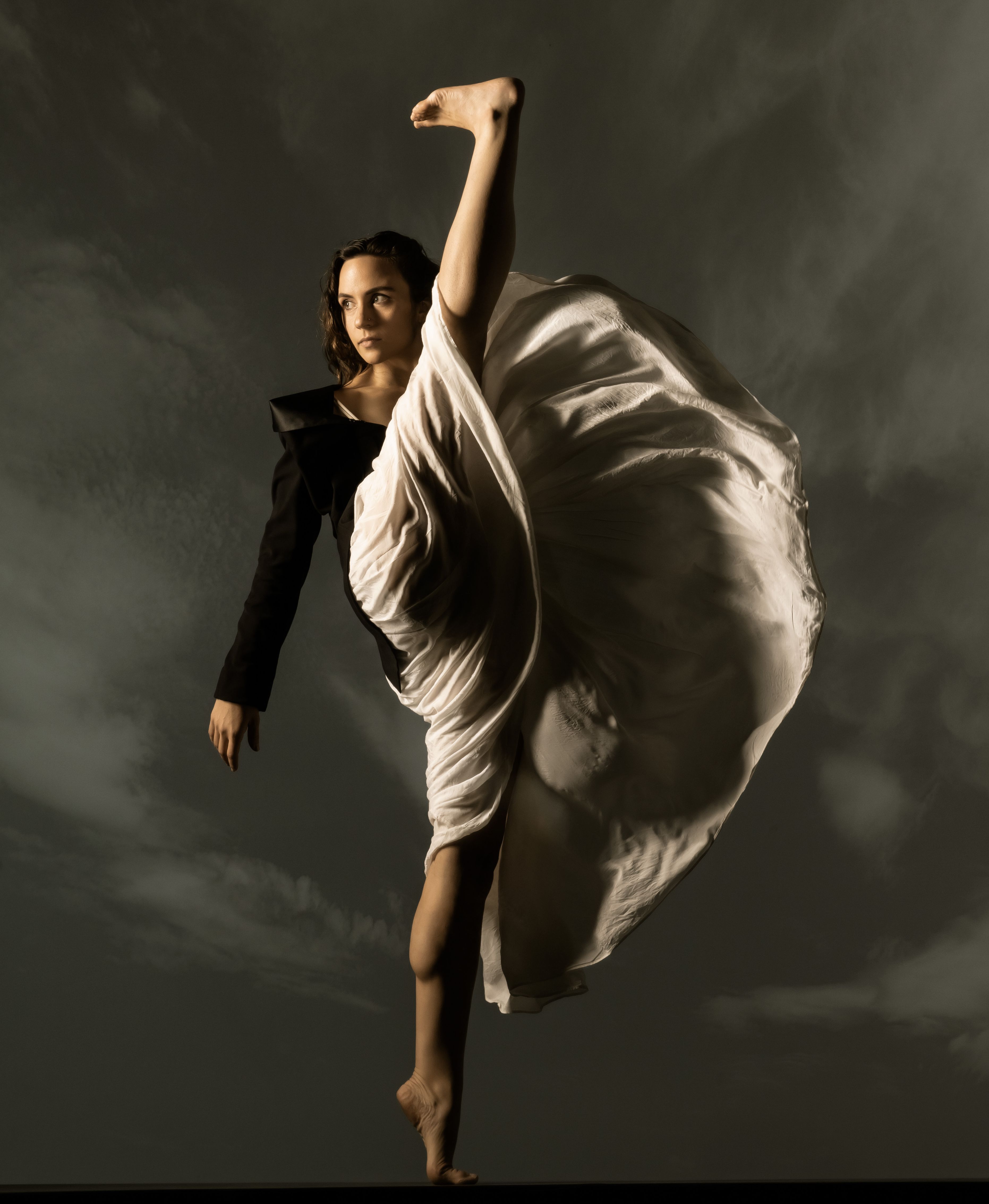 dancer in ivory colored billowing skirt kicks on leg above head
