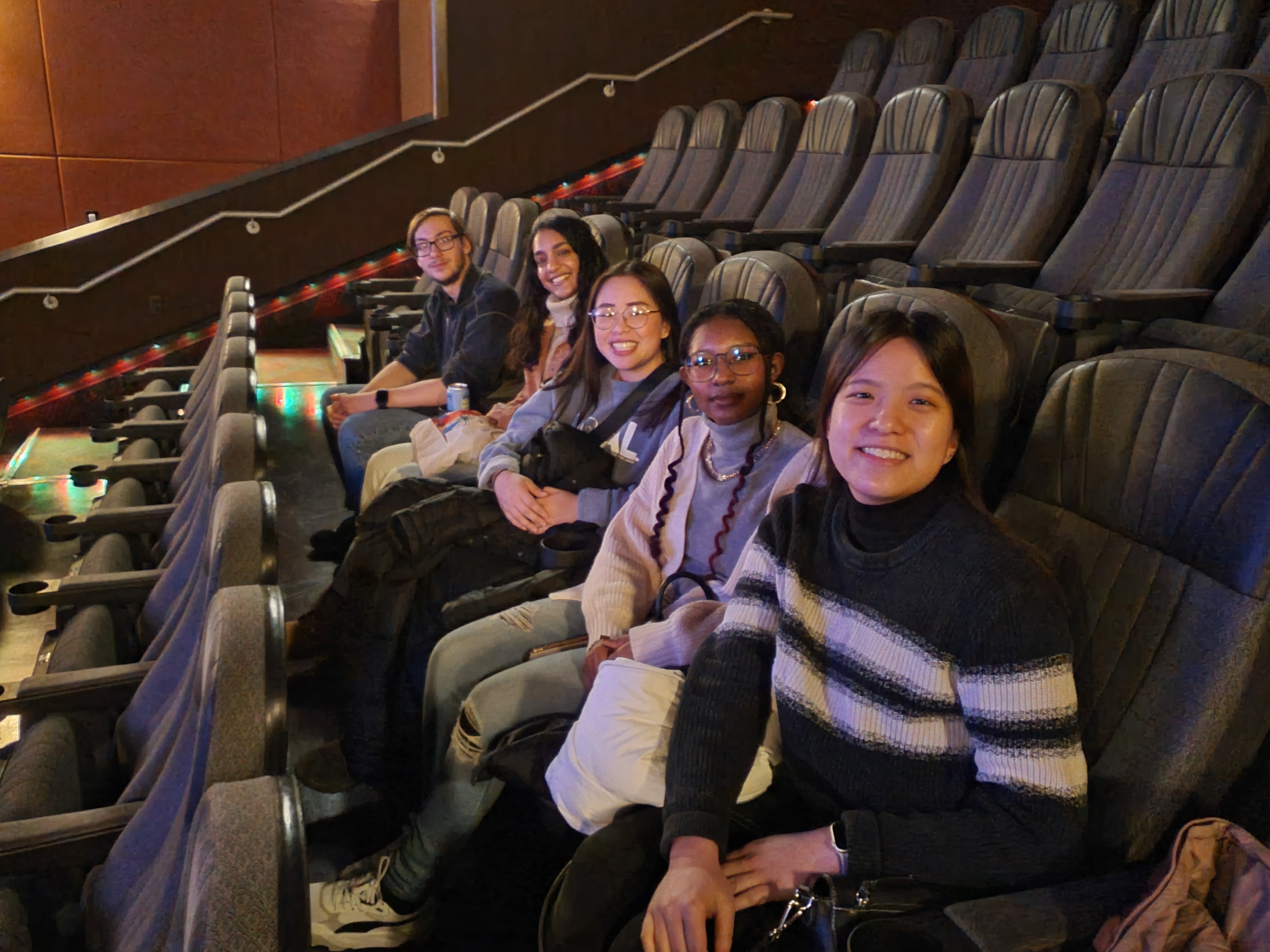 Students sit and smile in a row of seats at the movie theater.