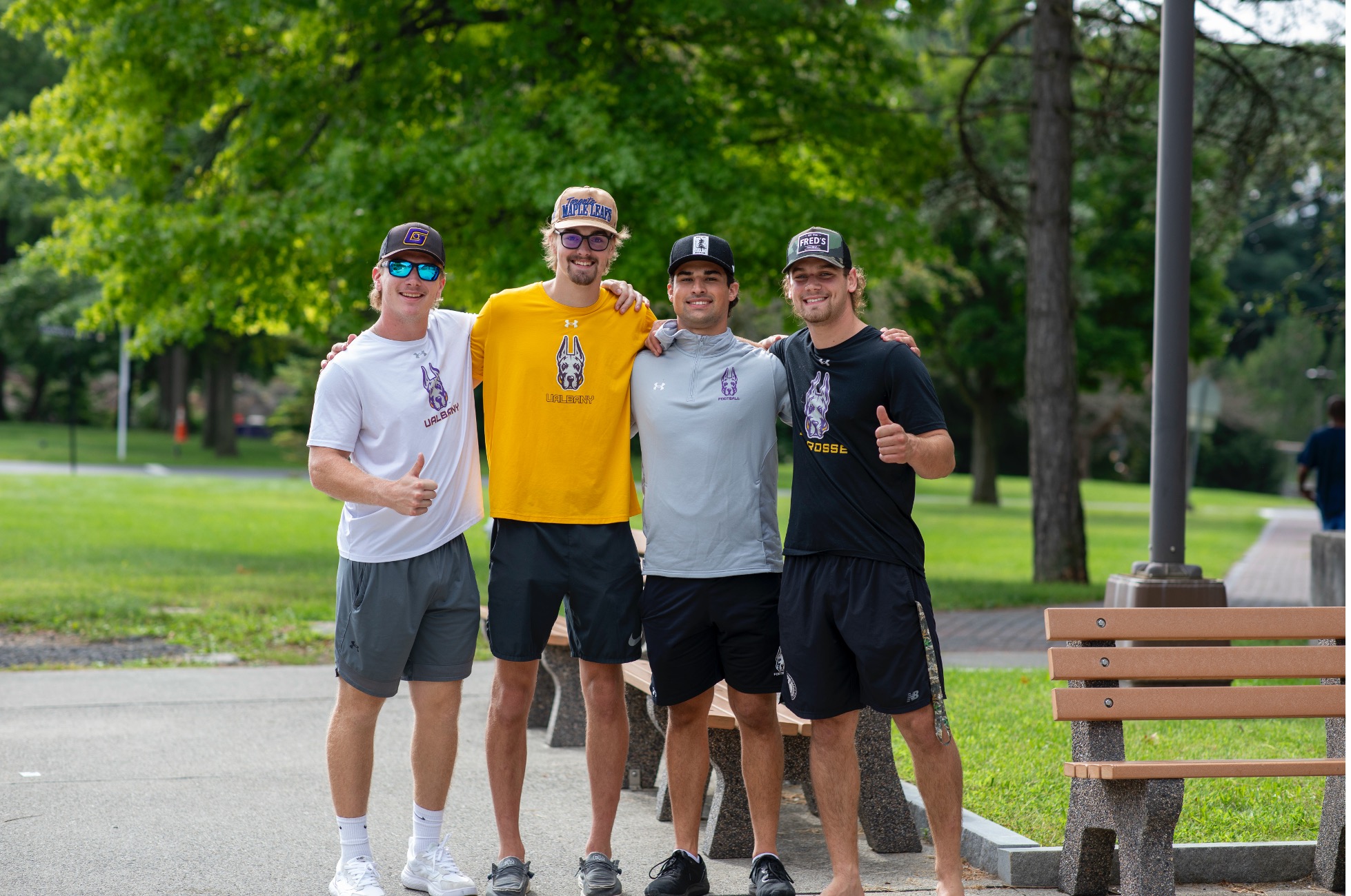 Four people stand, wearing UAlbany clothing and smiling as they pose for a photo.