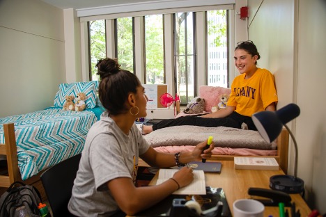 Two UAlbany tudents relax in their dorm room, talking to each other.