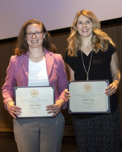 Two smiling women hold awards certificates