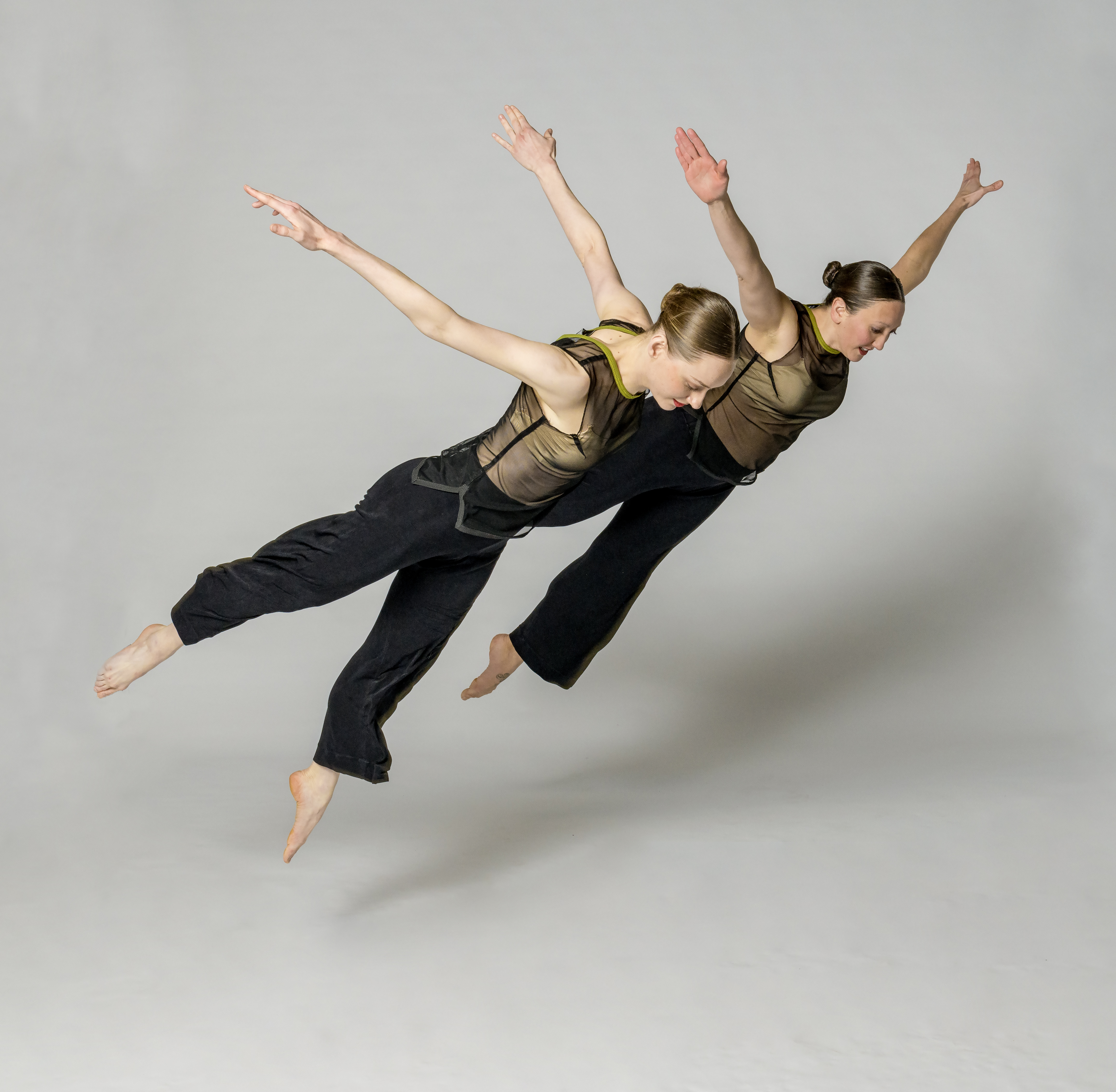 two dancers with arms raised overhead leap in the air while tilted forward