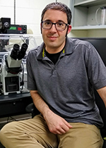 Jeremy Logue, friend of UAlbany's RNA Institute, sits beside a microscope