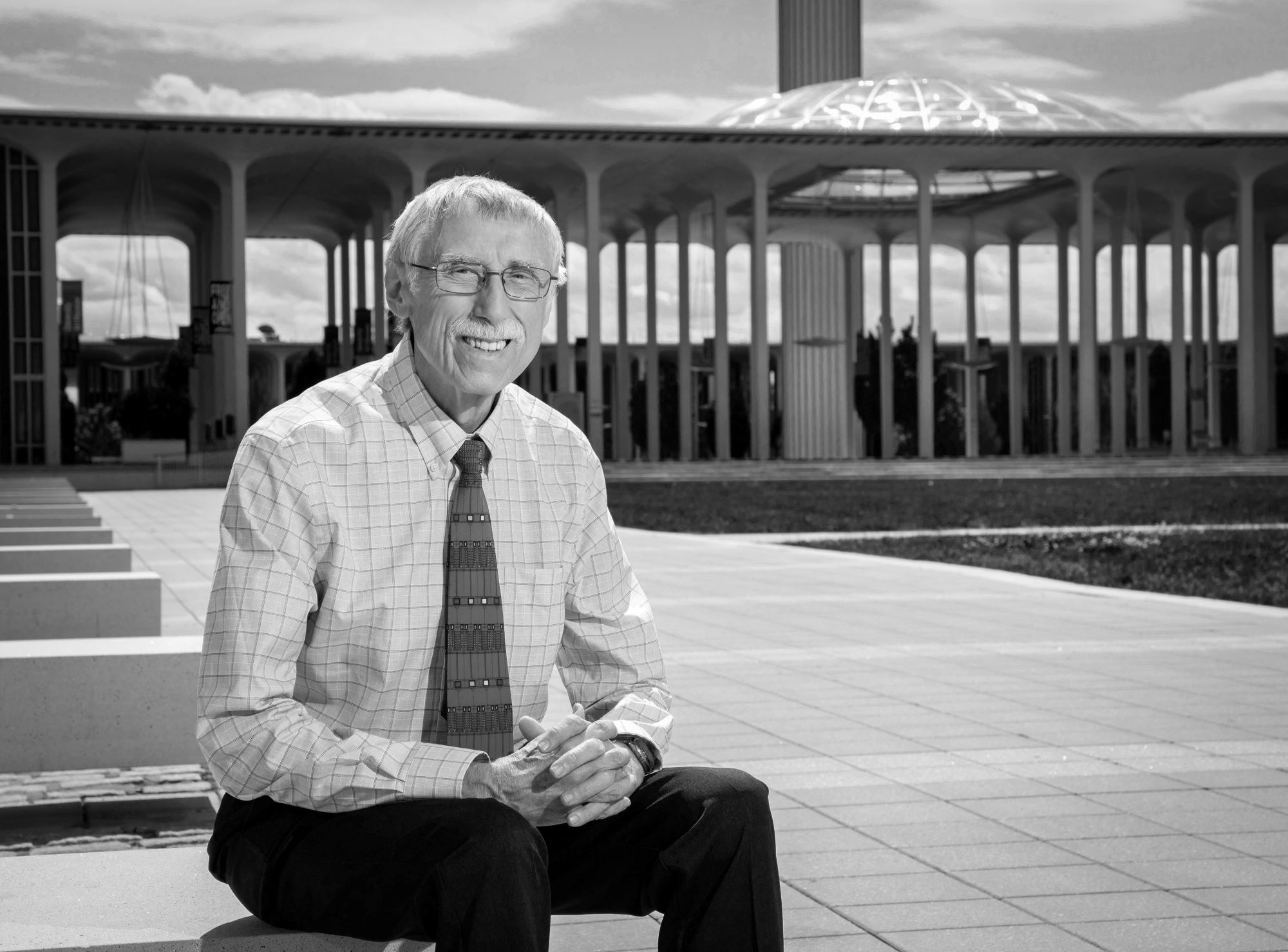 Ray Bromley sitting at Collins Circle with the UAlbany Academic Podium in the background