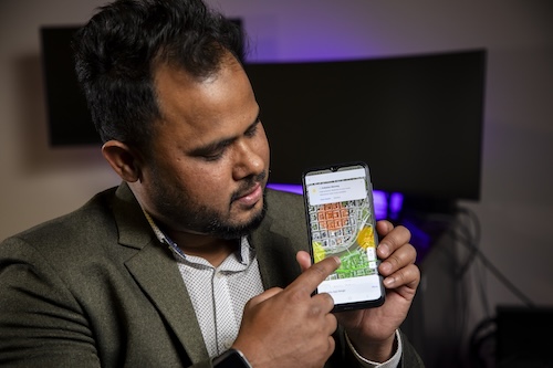 A man in a gray suit jacket points at a pollution map on his phone screen