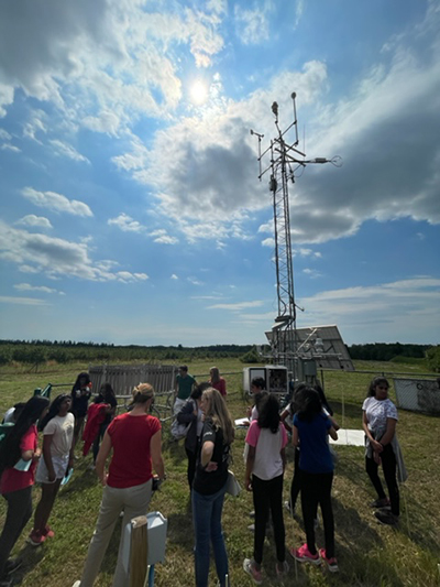 A group of girls surround the weather cluster at Mesonet outside in a field.