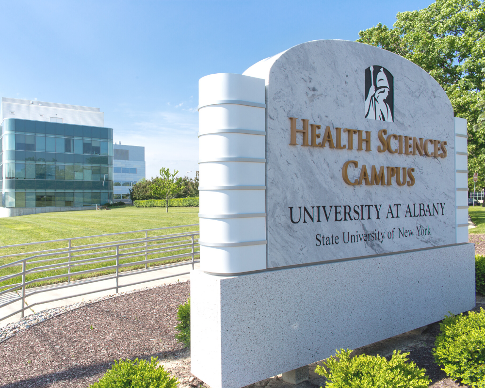 "Health Sciences campus" sign with a health science building, a blue sky, and bright green grass in the background.