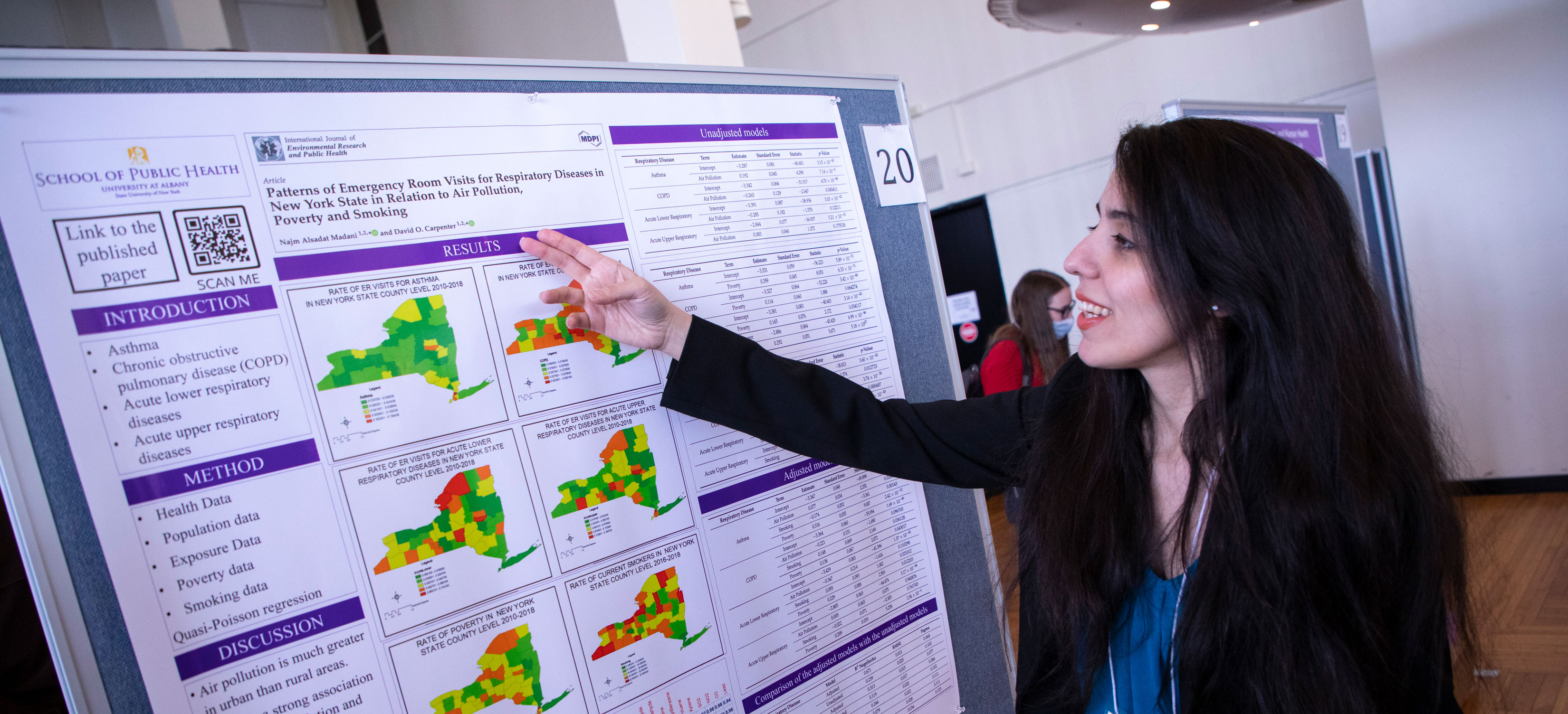 A student gestures toward a research poster board with colorful maps of New York State at a poster session at UAlbany Showcase.