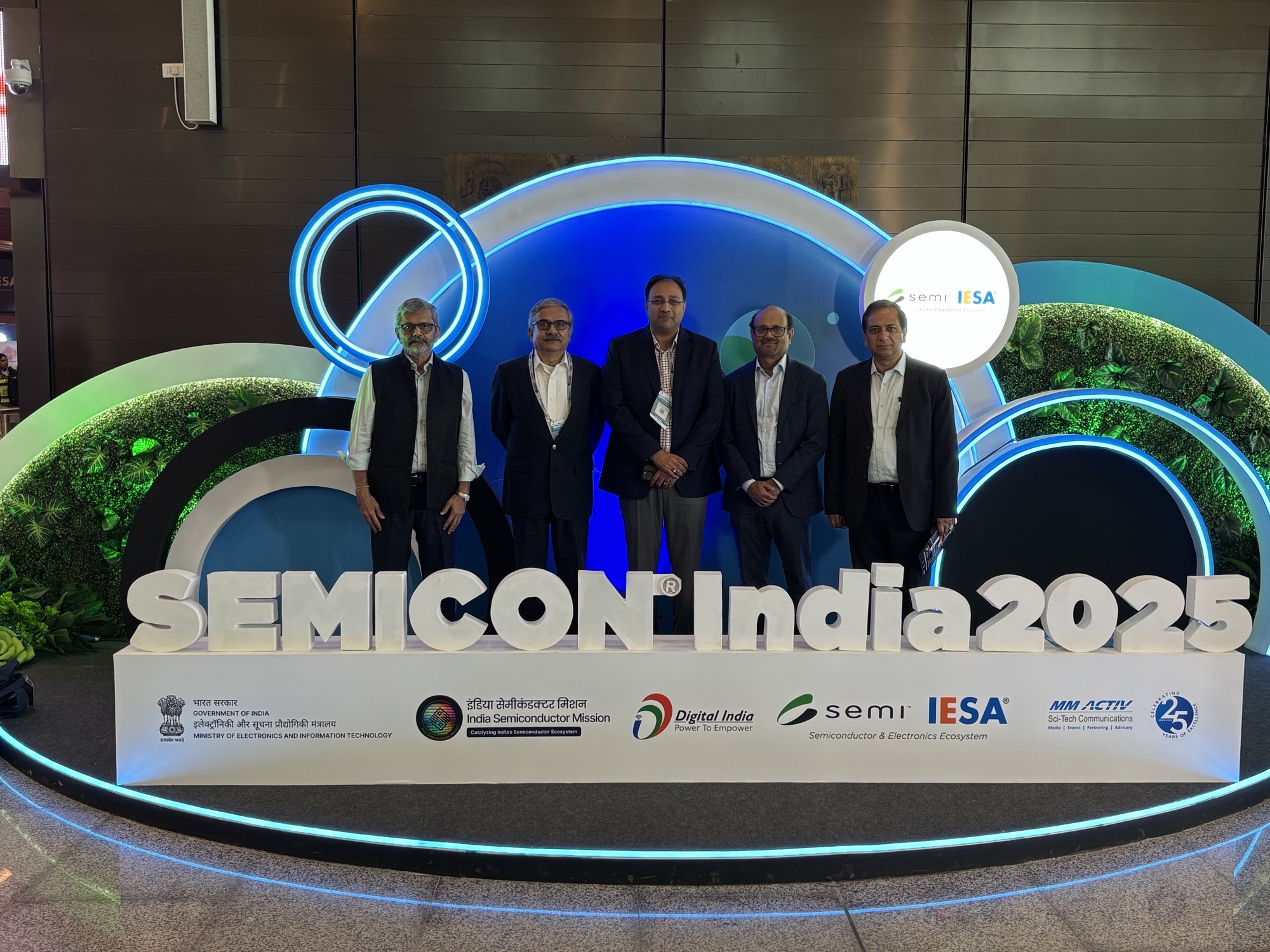 Five men pose in a line behind a white sign that says "Semicon India 2025"