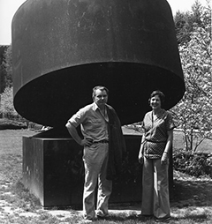 A man and woman stand before a wide 12-foot-high dark metal sculpture