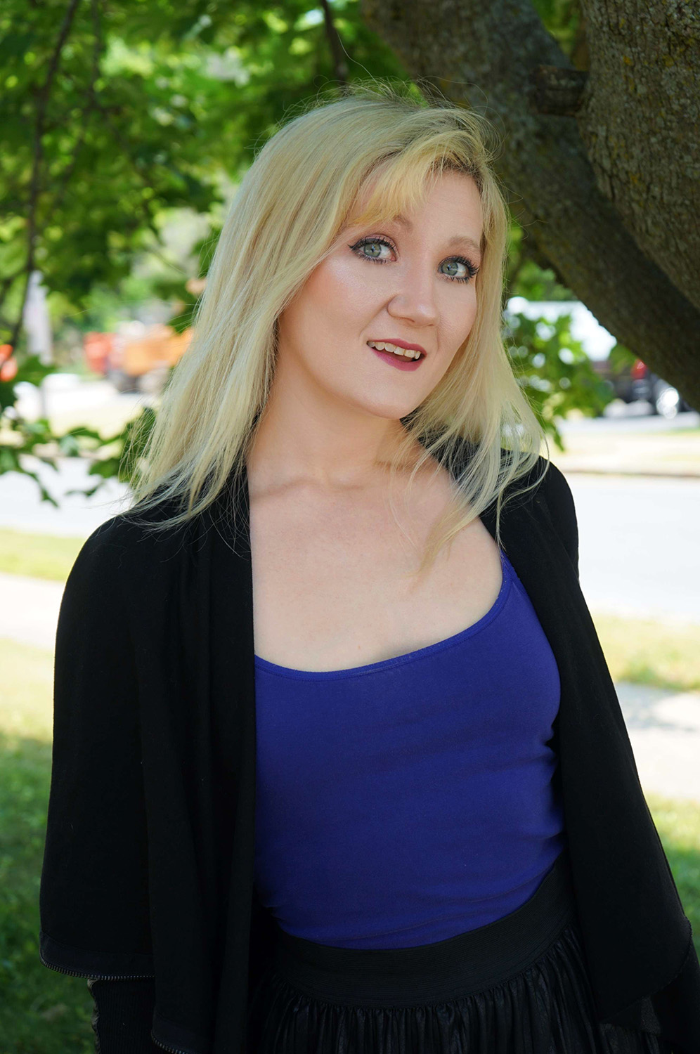 blonde woman in blue shirt and dark sweater under a tree