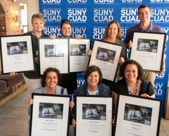 Seven smiling people hold framed awards.