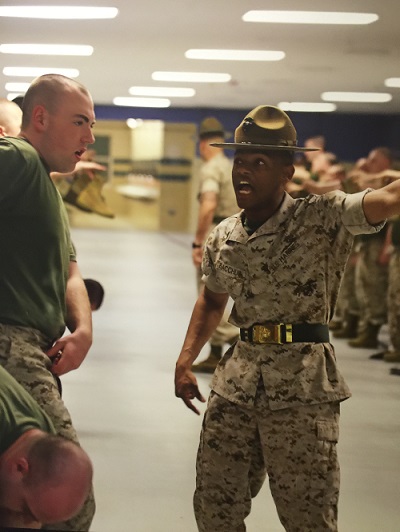 A uniformed Marine shouts and points off screen as a recruit listens nearby.