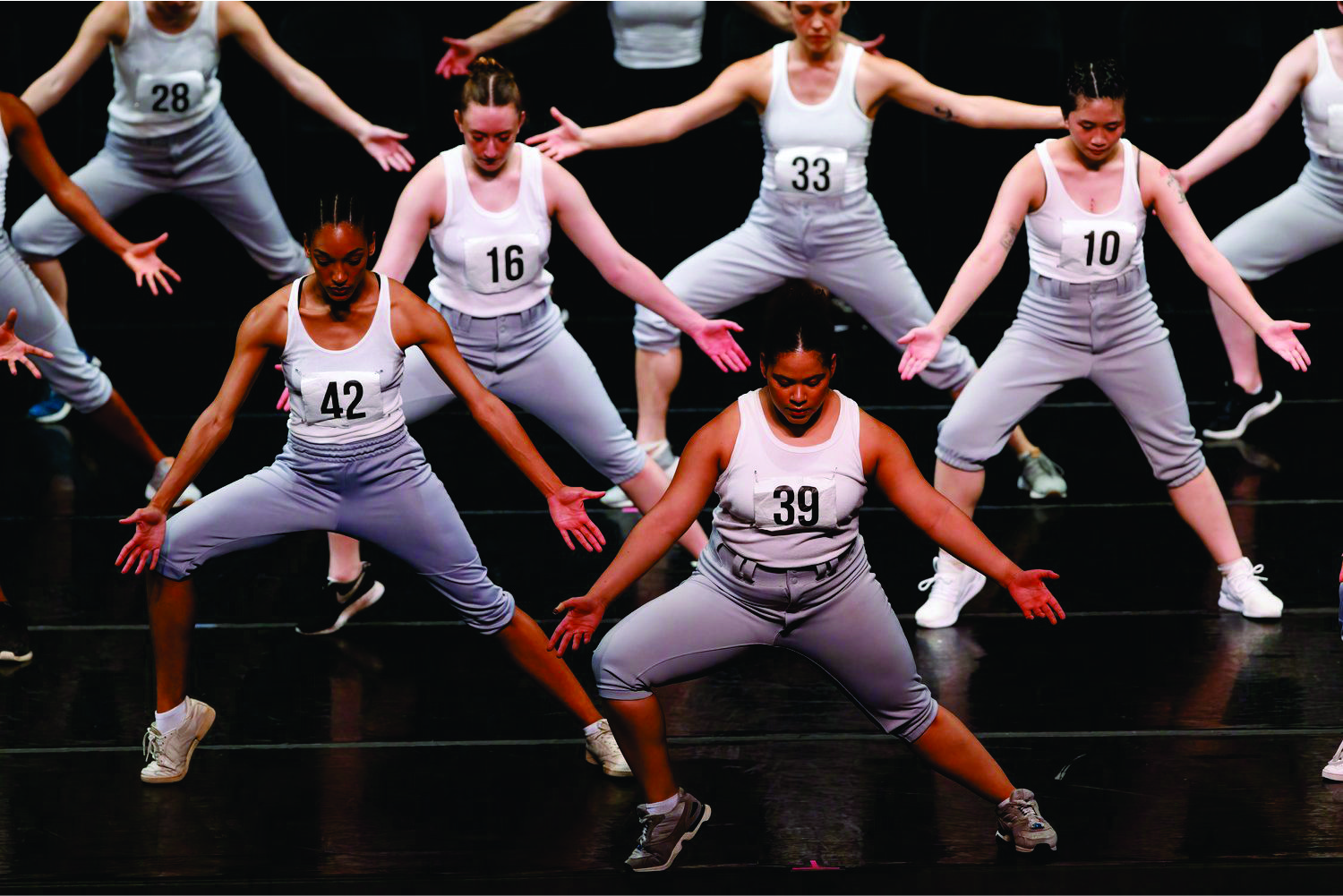 many dancers with numbers on their shirts stand with arms and legs spread