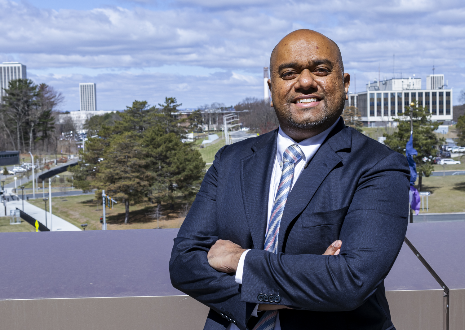 a man in a blue suit smiles, arms crossed