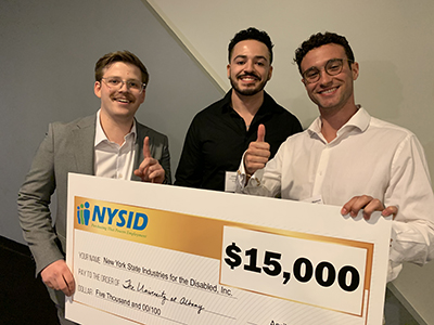 Three students stand with a $15,000 check from NYSID for their first-place project to help people working with disabilities.