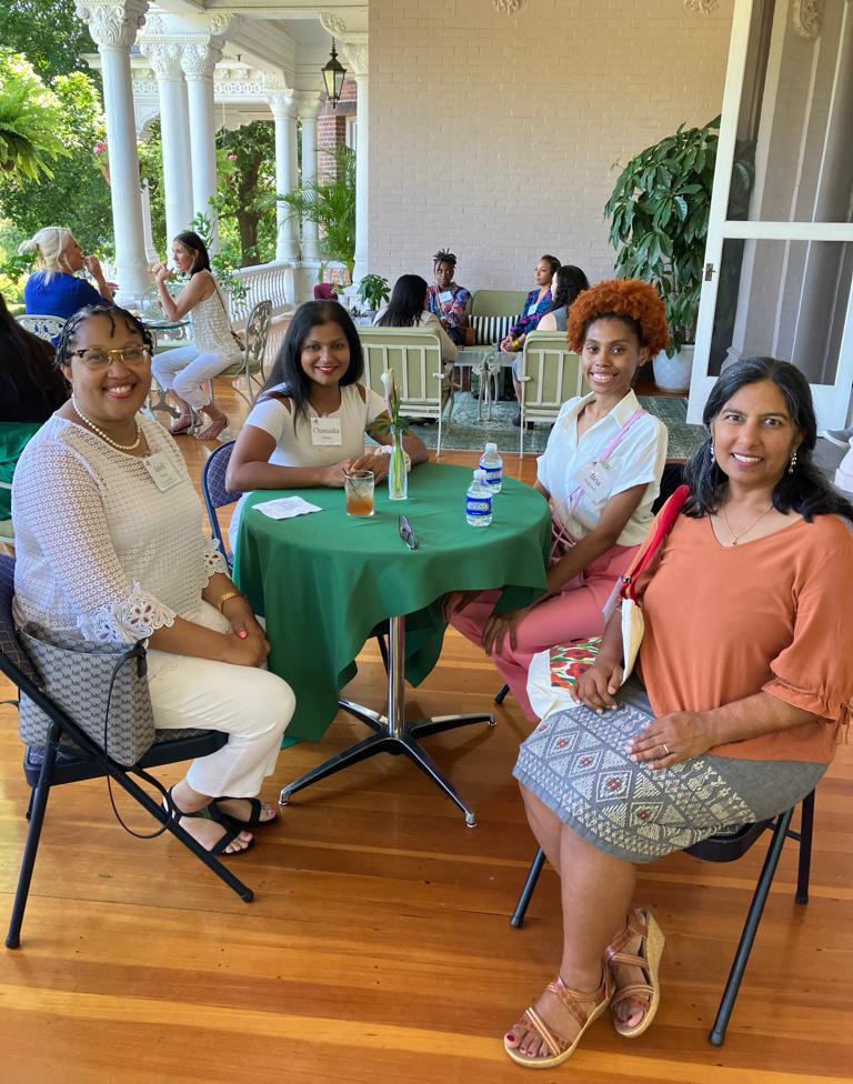 Four WGSS faculty and students smile at the camera while seated at a table on the porch of the Governor's Mansion.