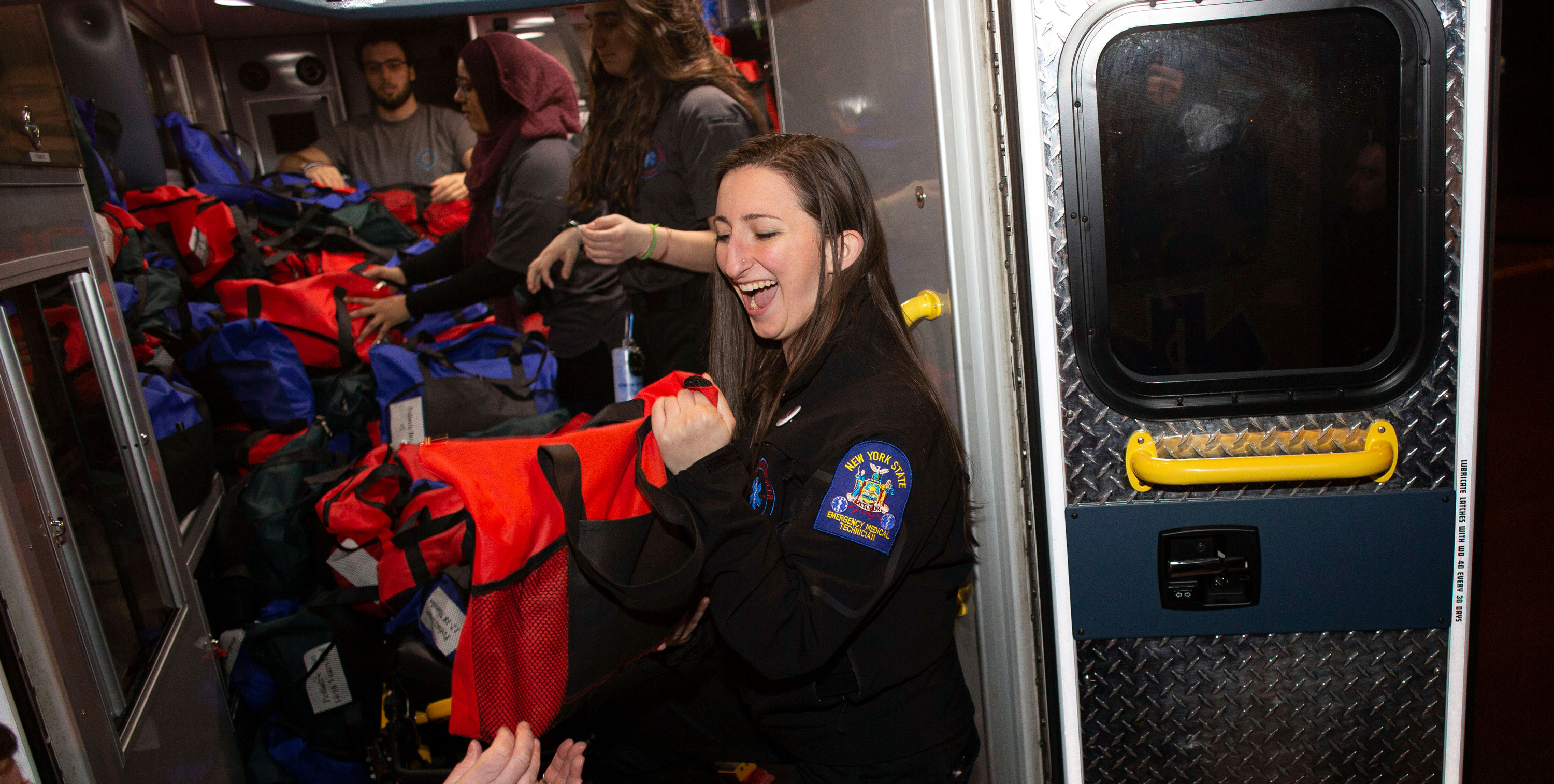 A Five Quad Ambulance volunteer smiles as she hands off a duffel bag and grabs another as the group loads up an ambulance with donated supplies.
