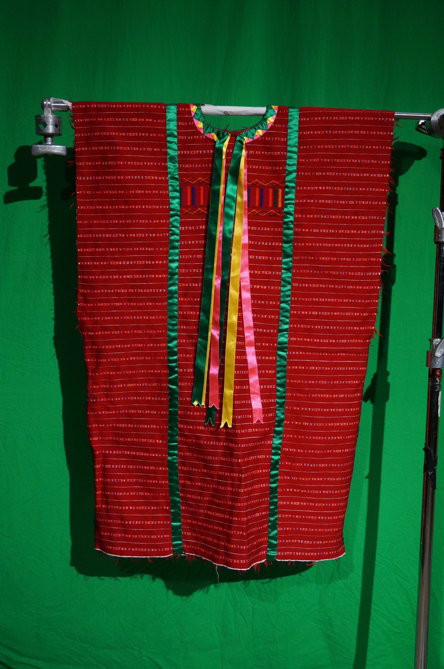 A woman's red fabric huipil with green, yellow and pink silk ribbons.