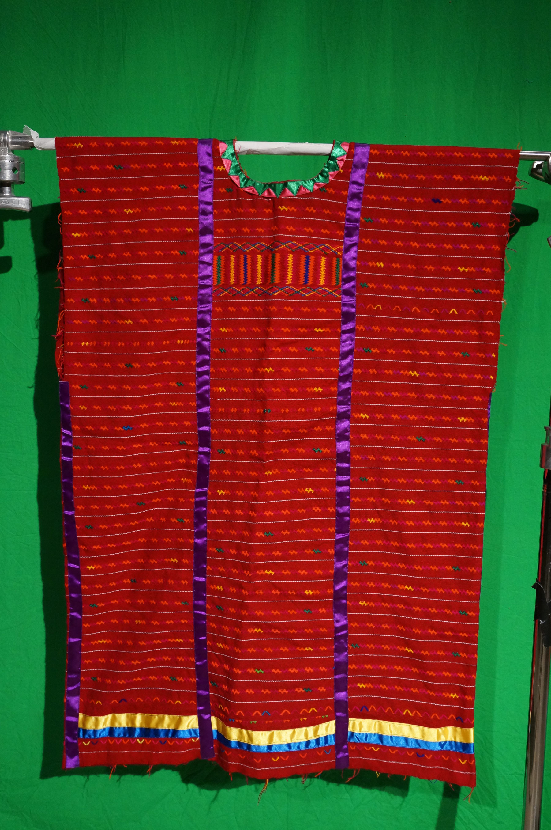 A woman's red fabric huipil with purple, yellow and blue silk ribbons.