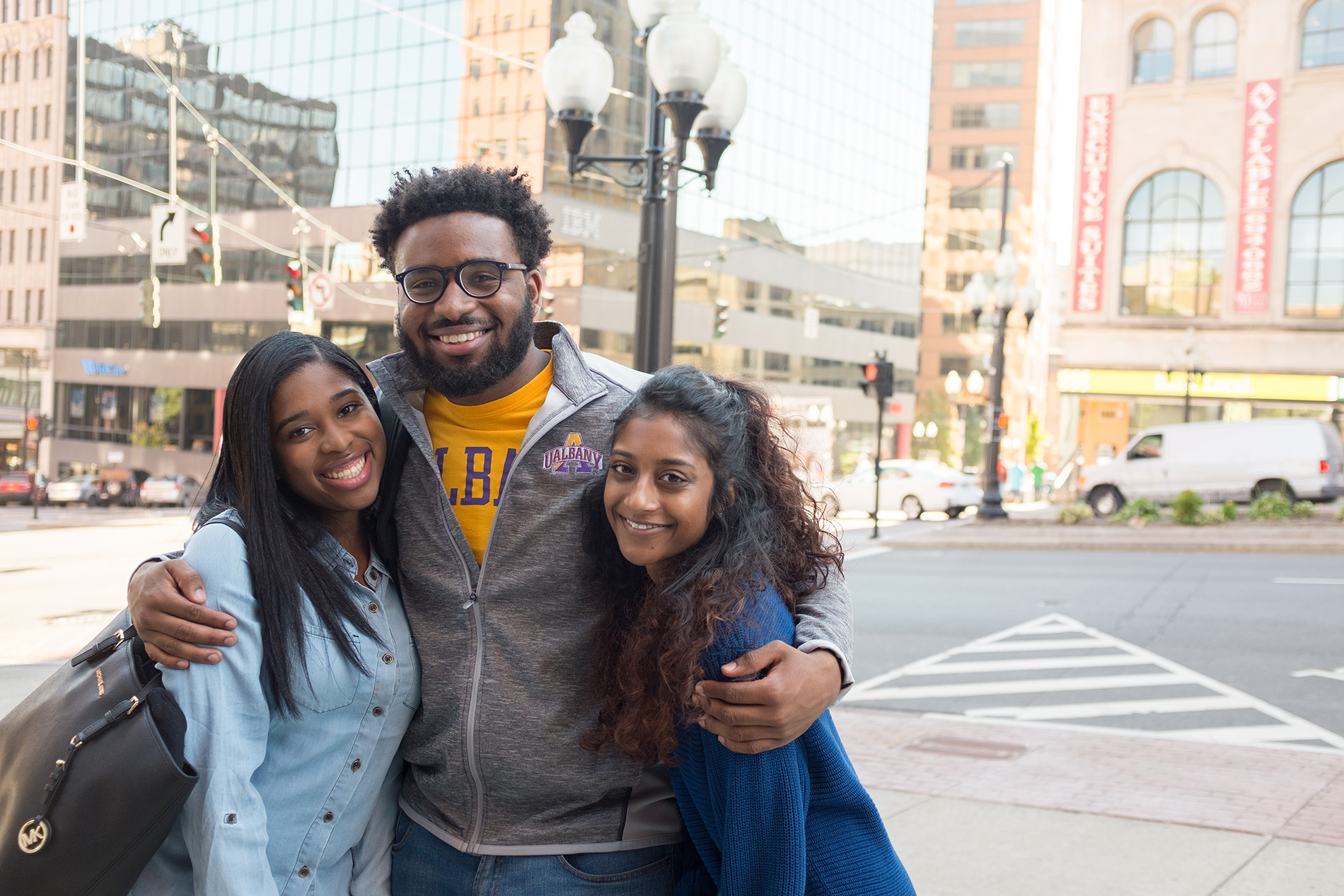 Three students stand on an Albany street, smiling at the camera.