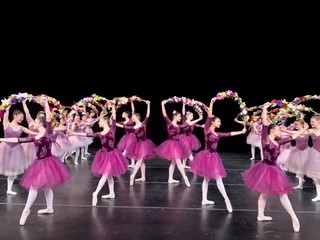 A group of dancers in pink outfits perform on stage.