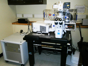 An array of white microscopic equipment sits on a black table, with an eyepiece, and wires coming out of the sides.