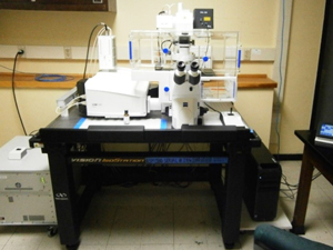An array of white microscopic equipment sits on a black table, with an eyepiece, and wires coming out of the sides.