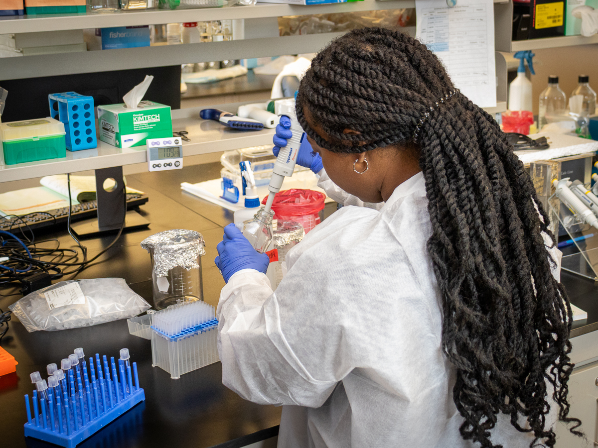 Ariana Nobles in the Mantis Lab at Wadsworth. She wears a white protective coat and blue latex gloves.
