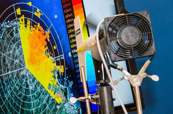 Weather prediction hardware in front of a screen showing a colorful forecasting chart.