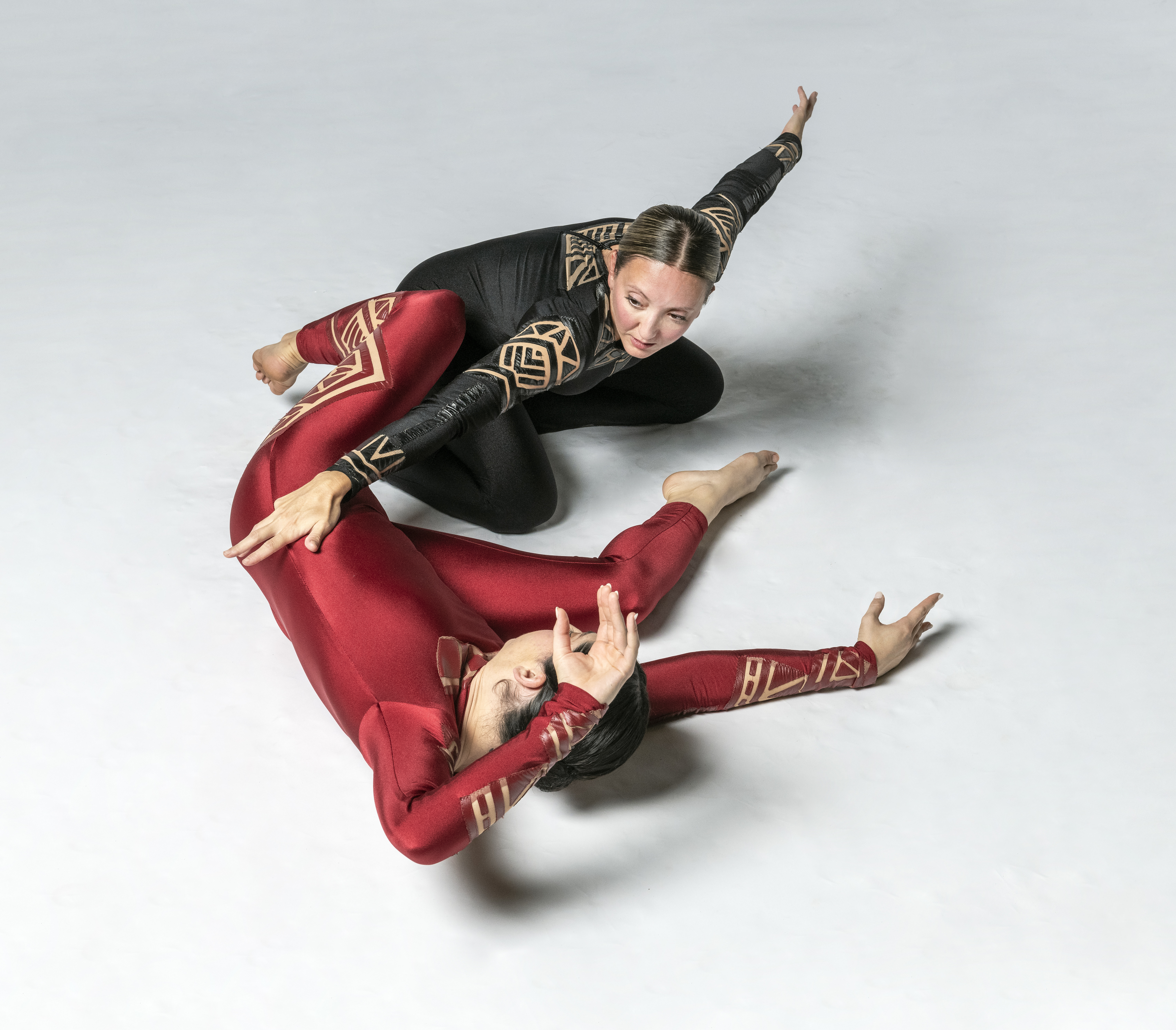 two dancers on floor are linked through extended arms and legs