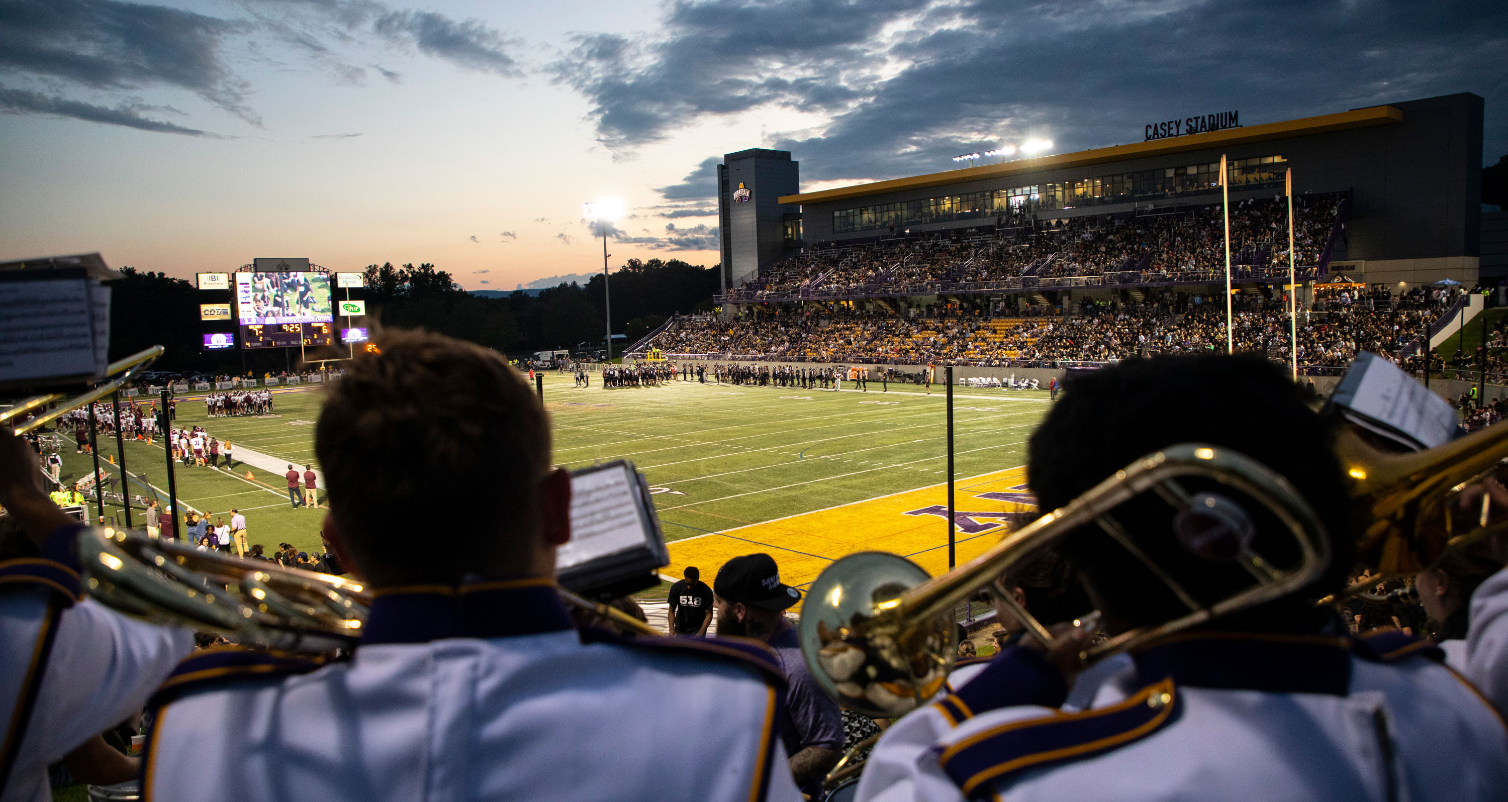 The Marching Great Danes perform in uniform on the edge of the field at Casey Stadium at sunset.
