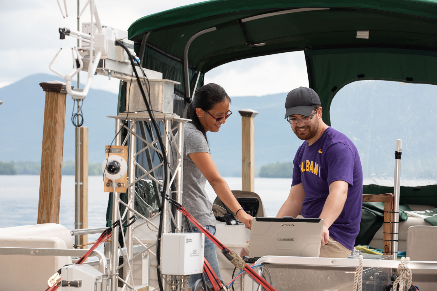 Two researchers aboard a boat examining data on a laptop while conducting fieldwork on a lake.