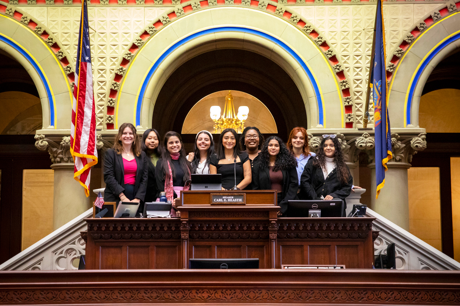 A group of students standing inside a chamber of the New York State Capitol Building.