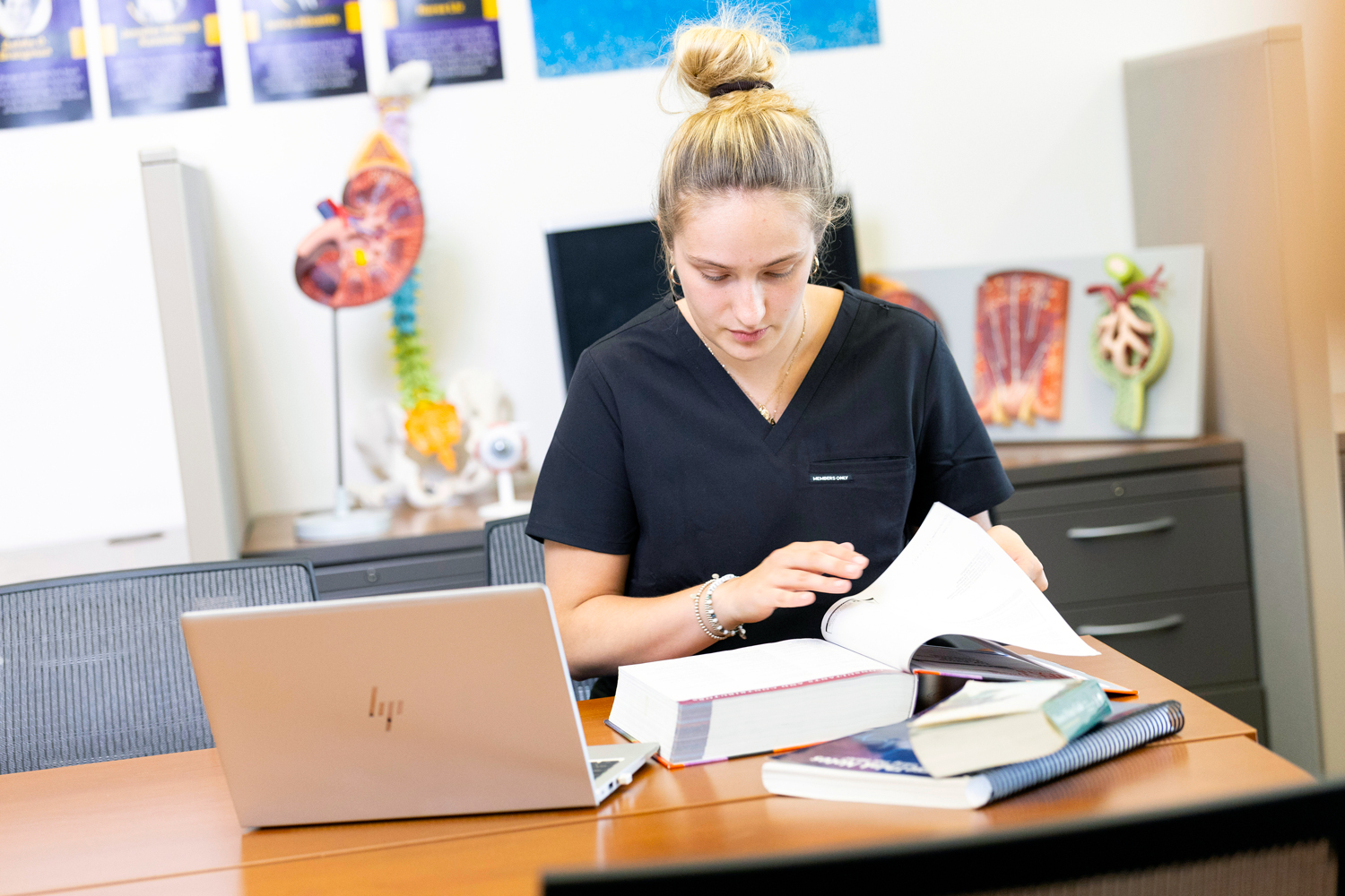 A nursing student studying with textbooks and a laptop.