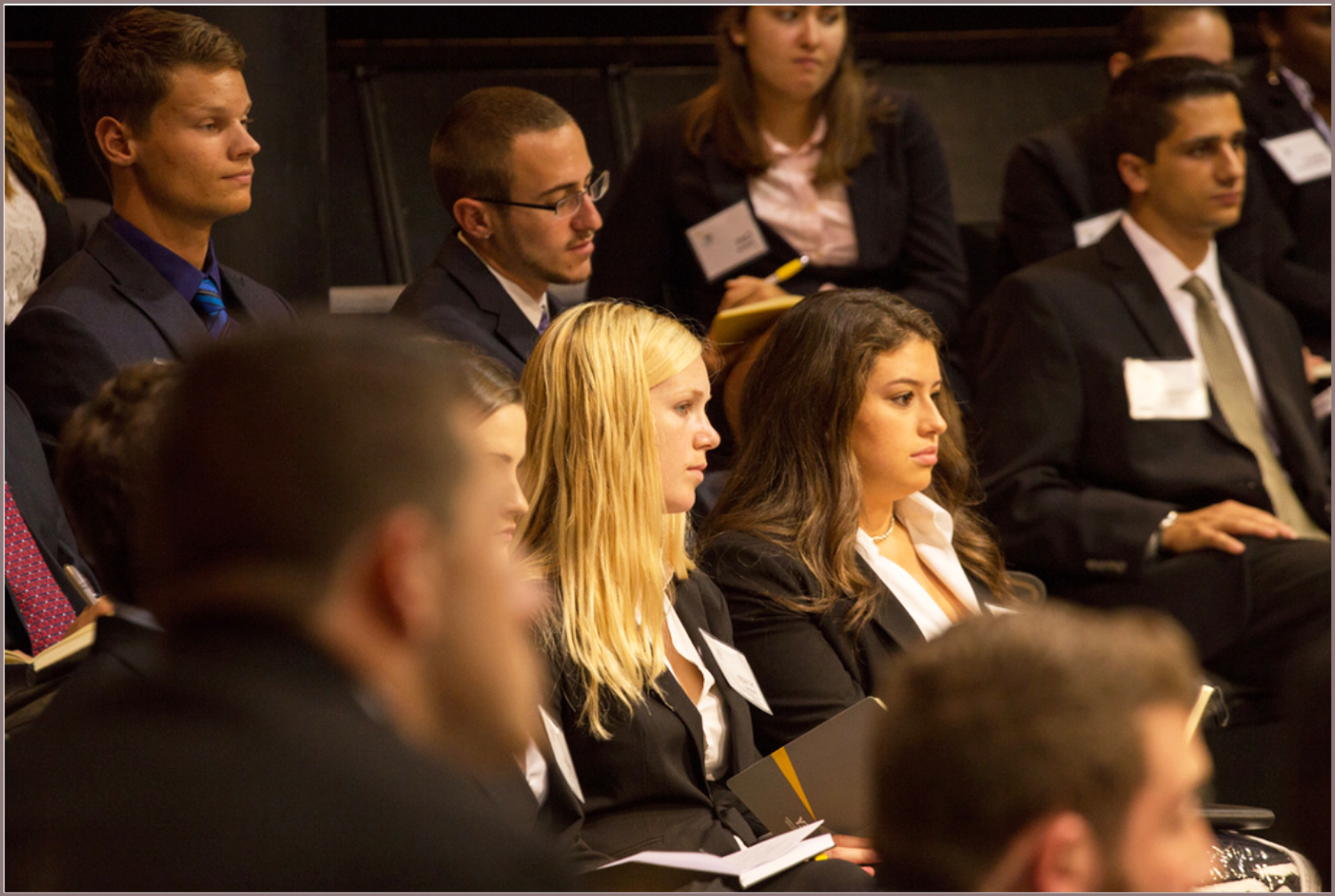 A group of business students wearing suits and name tags attending a lecture.