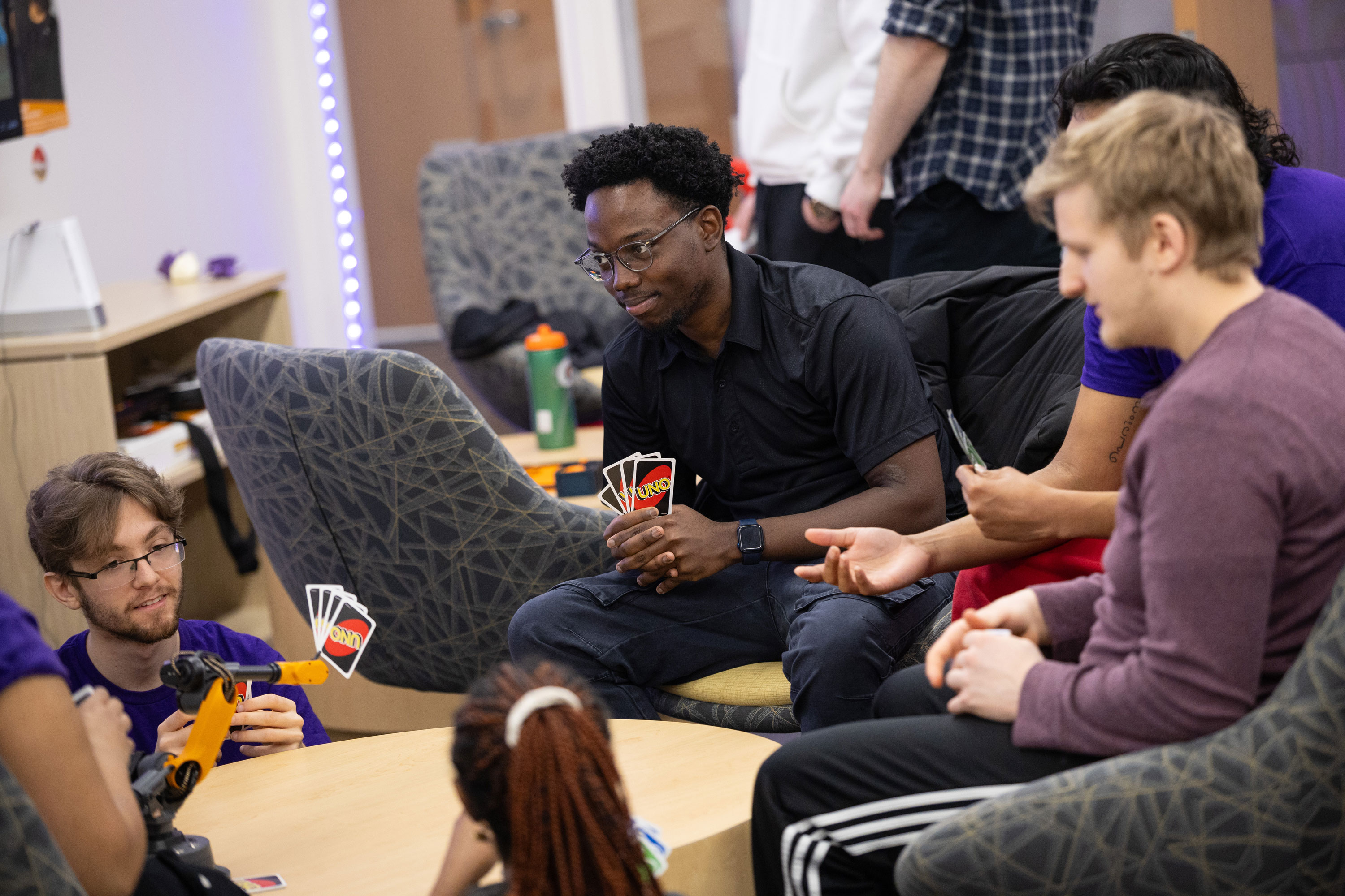 A group of students gathers around a table to play the card game Uno.