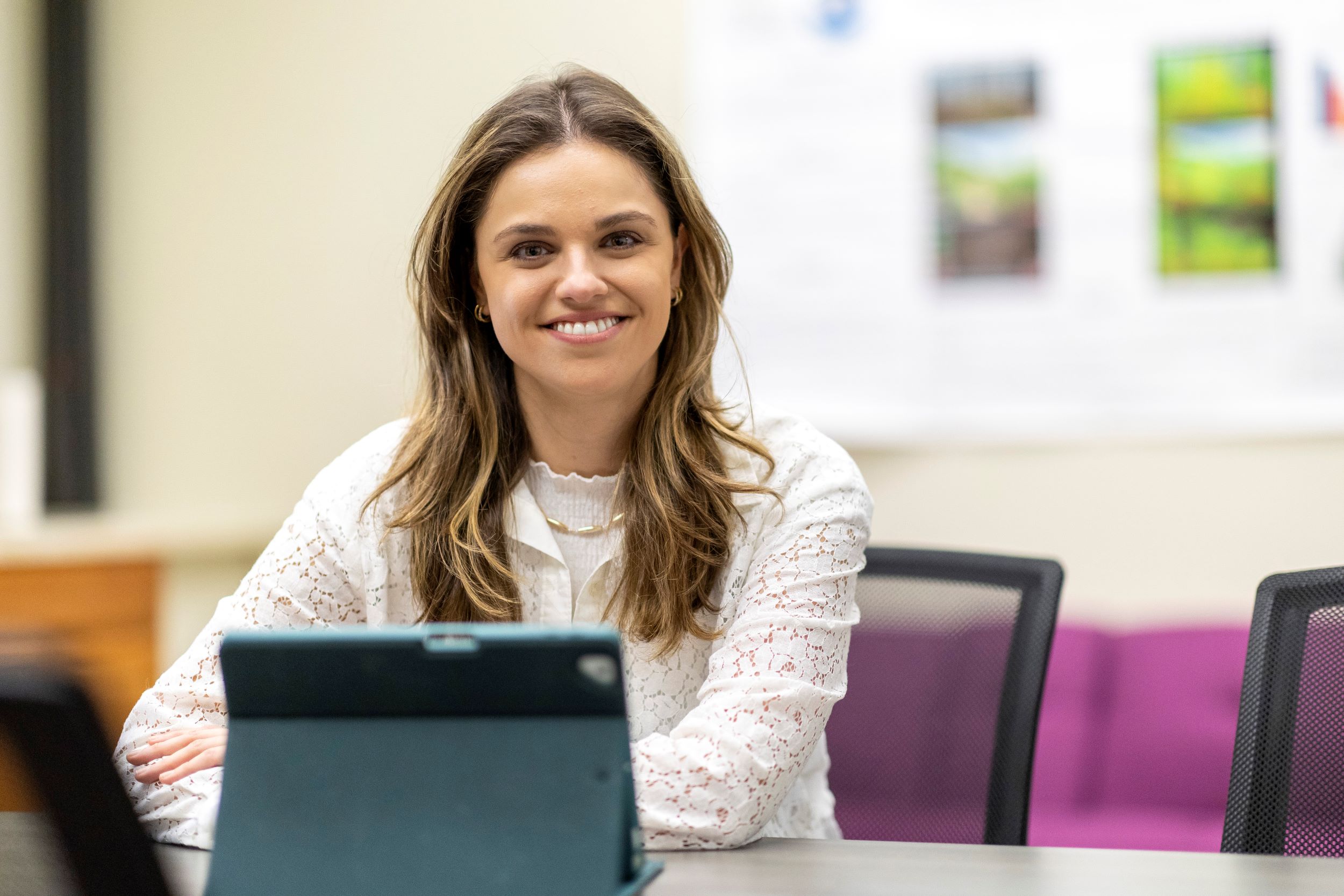 UAlbany doctoral student Caroline Rafizadeh, a Cognitive Psychology PhD Student, sits at a desk wearing a white shirt and a smile indoors.