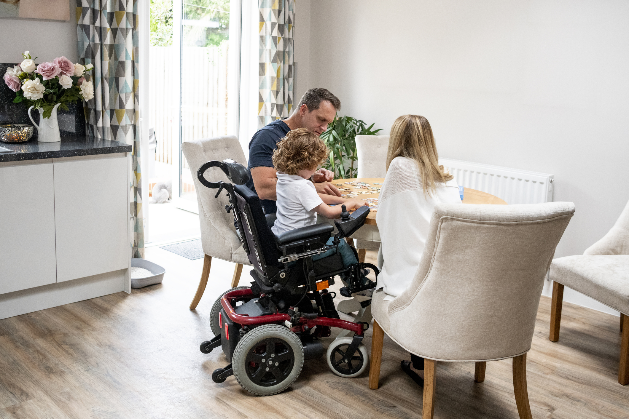 A child in a wheelchair working on a puzzle with two adults