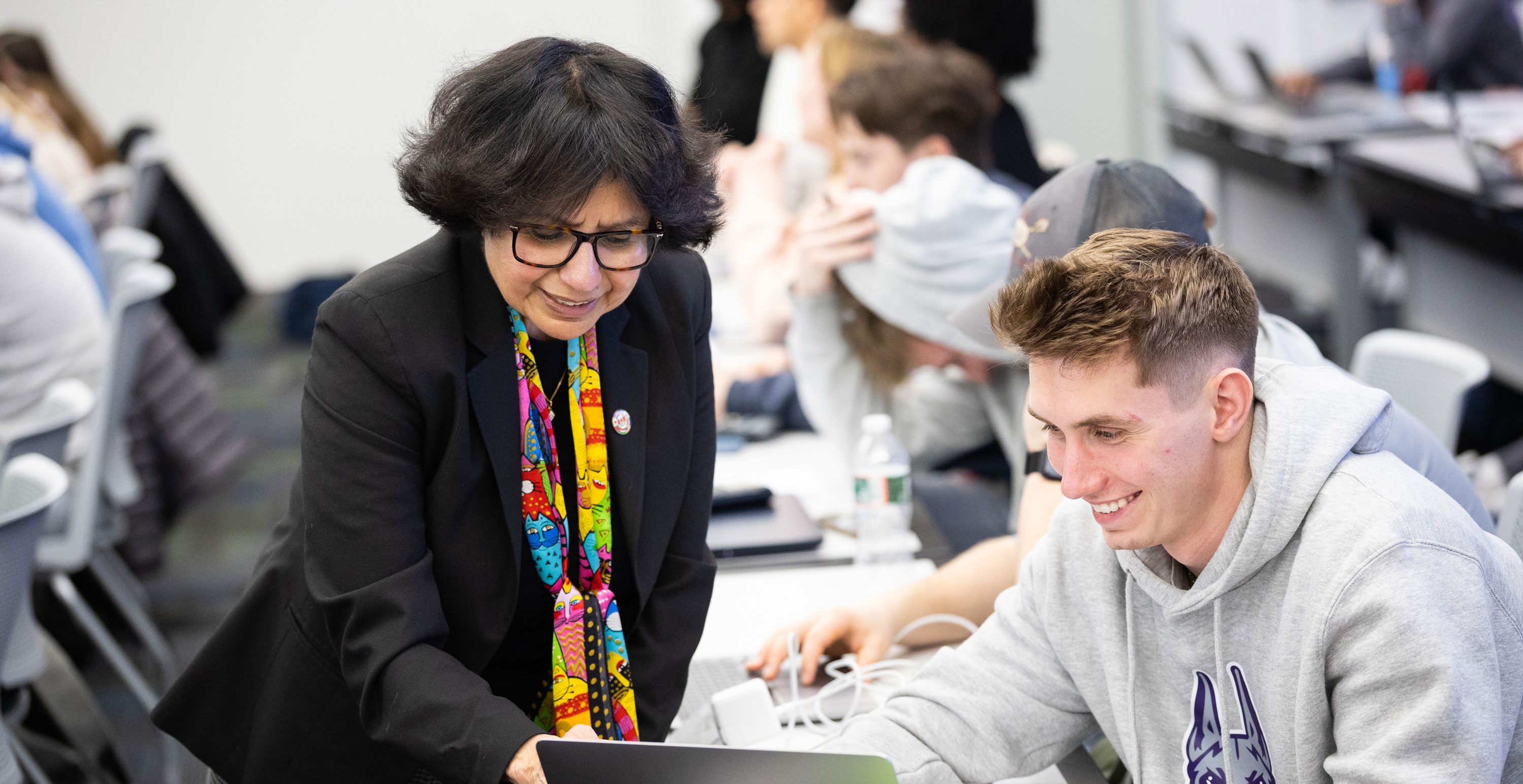 A faculty member and a student smile as they talk about something on the student's laptop screen.